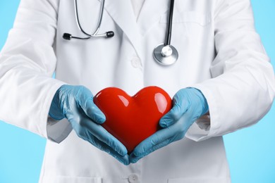 Doctor with red heart on light blue background, closeup