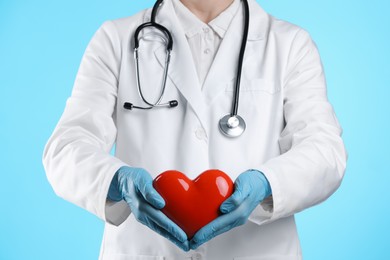 Photo of Doctor with red heart on light blue background, closeup