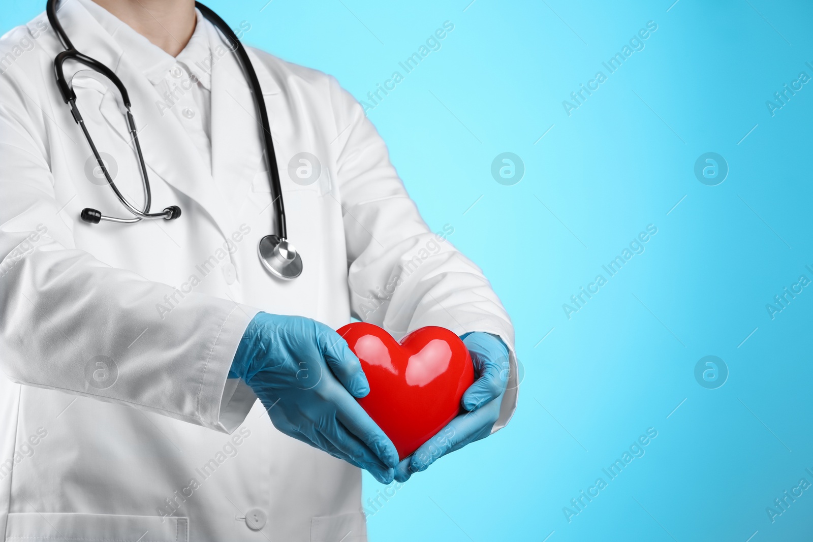 Photo of Doctor with red heart on light blue background, closeup. Space for text