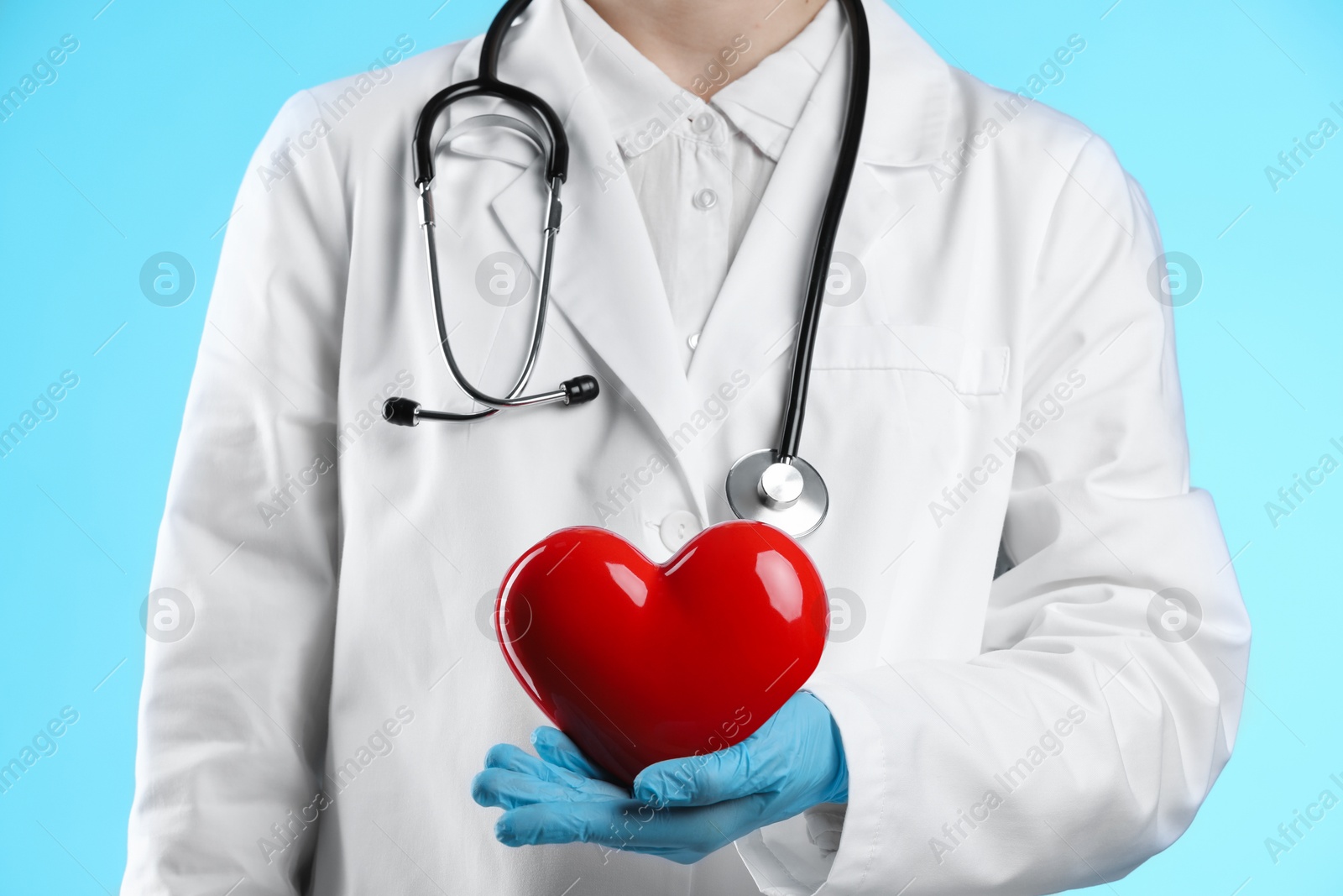 Photo of Doctor with red heart on light blue background, closeup