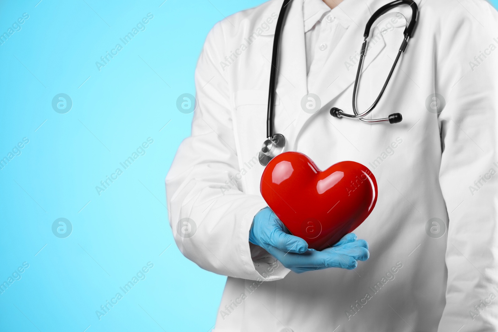 Photo of Doctor with red heart on light blue background, closeup. Space for text