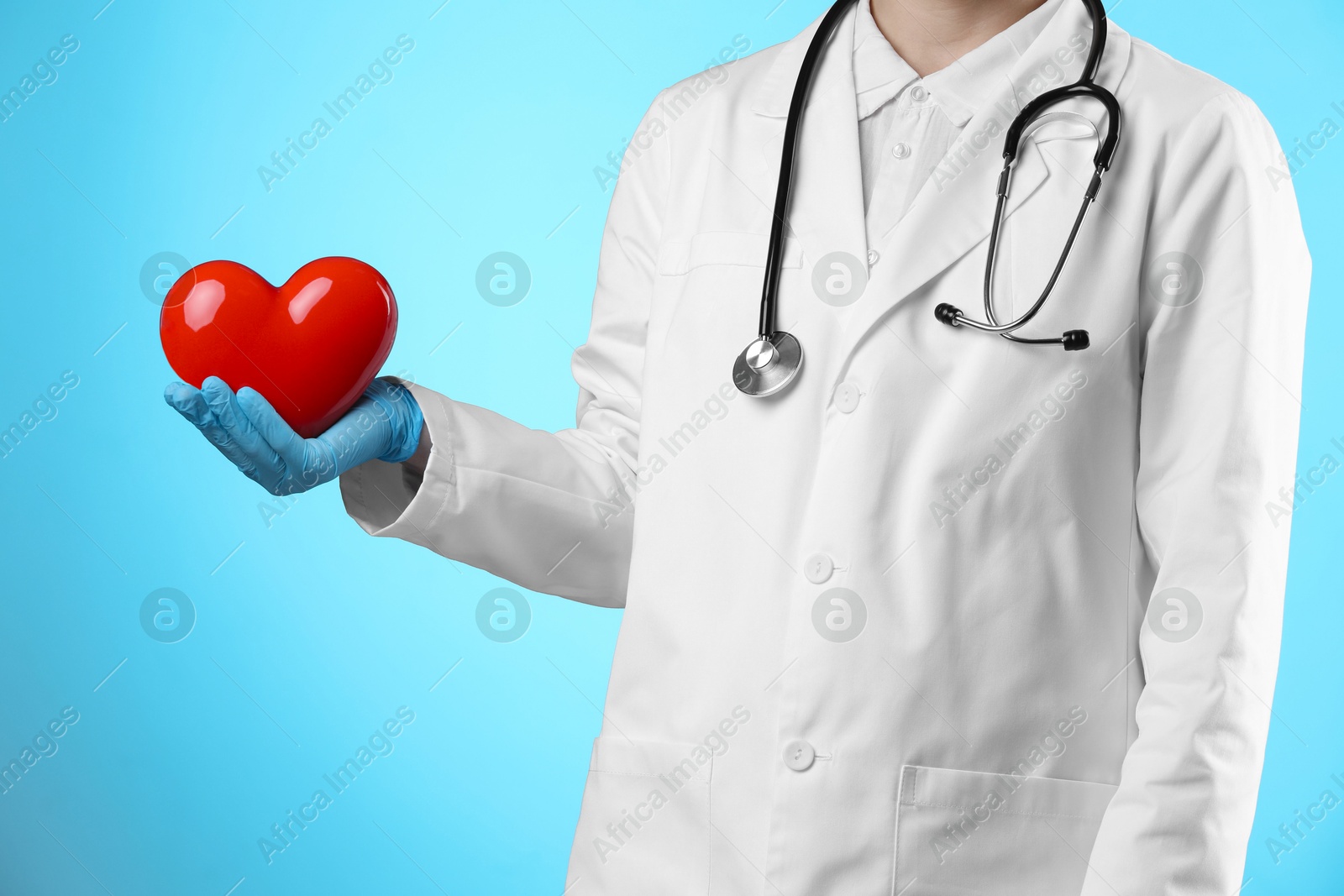 Photo of Doctor with red heart on light blue background, closeup