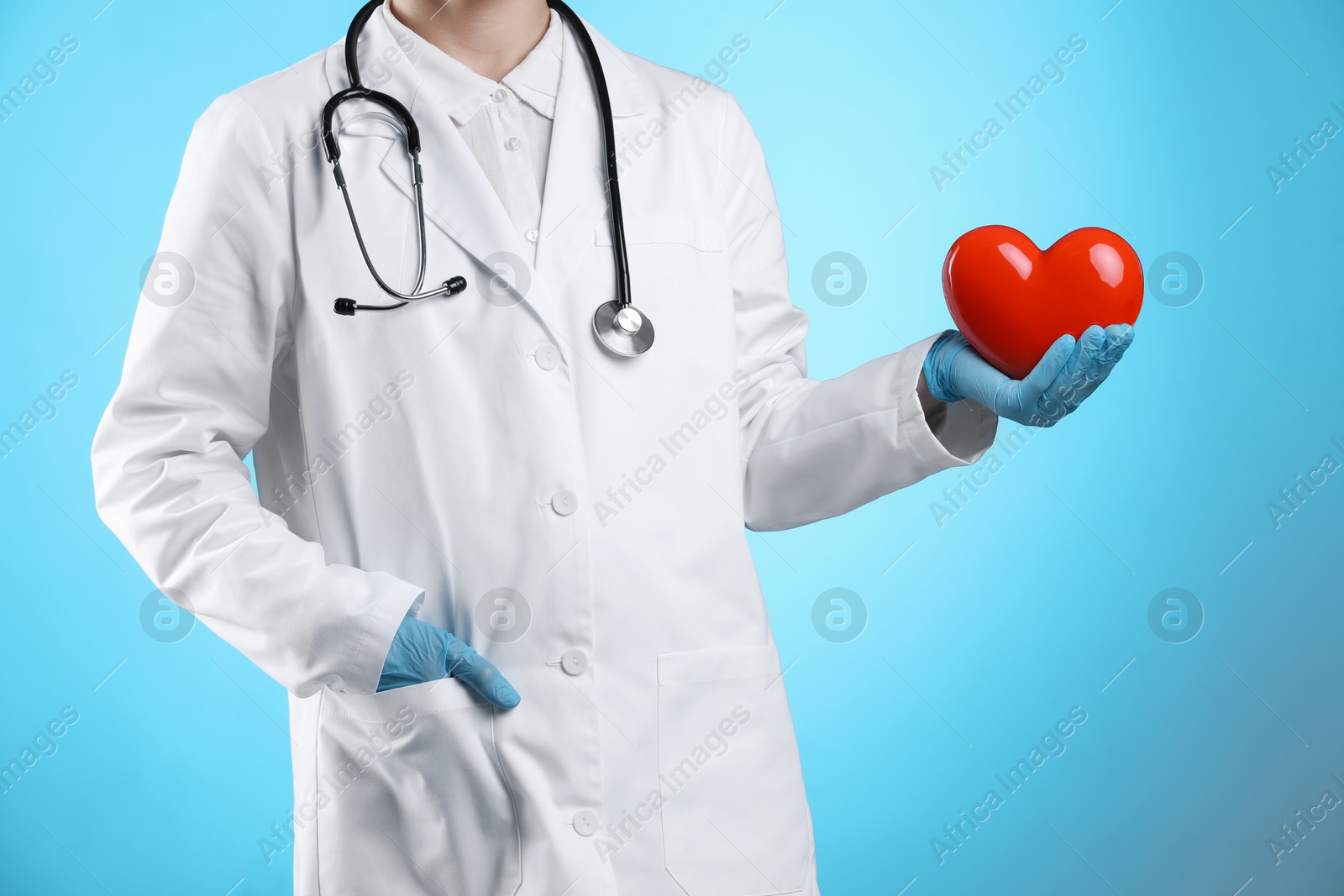 Photo of Doctor with red heart on light blue background, closeup