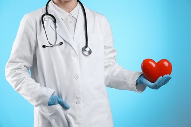 Doctor with red heart on light blue background, closeup