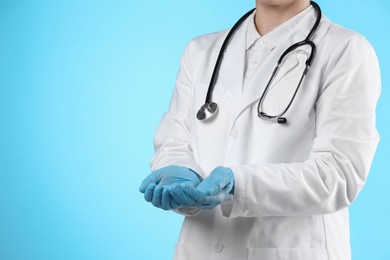 Doctor holding something on light blue background, closeup. Space for text