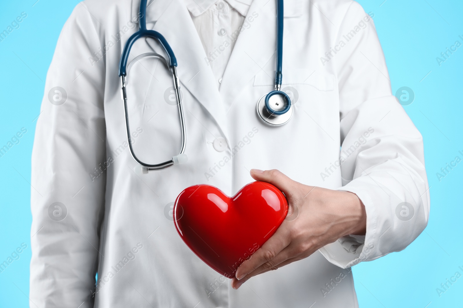 Photo of Doctor with red heart on light blue background, closeup