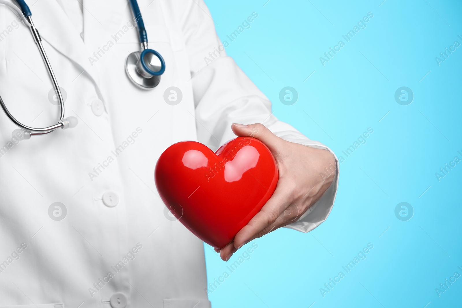 Photo of Doctor with red heart on light blue background, closeup