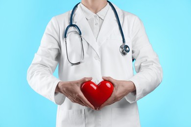 Photo of Doctor with red heart on light blue background, closeup