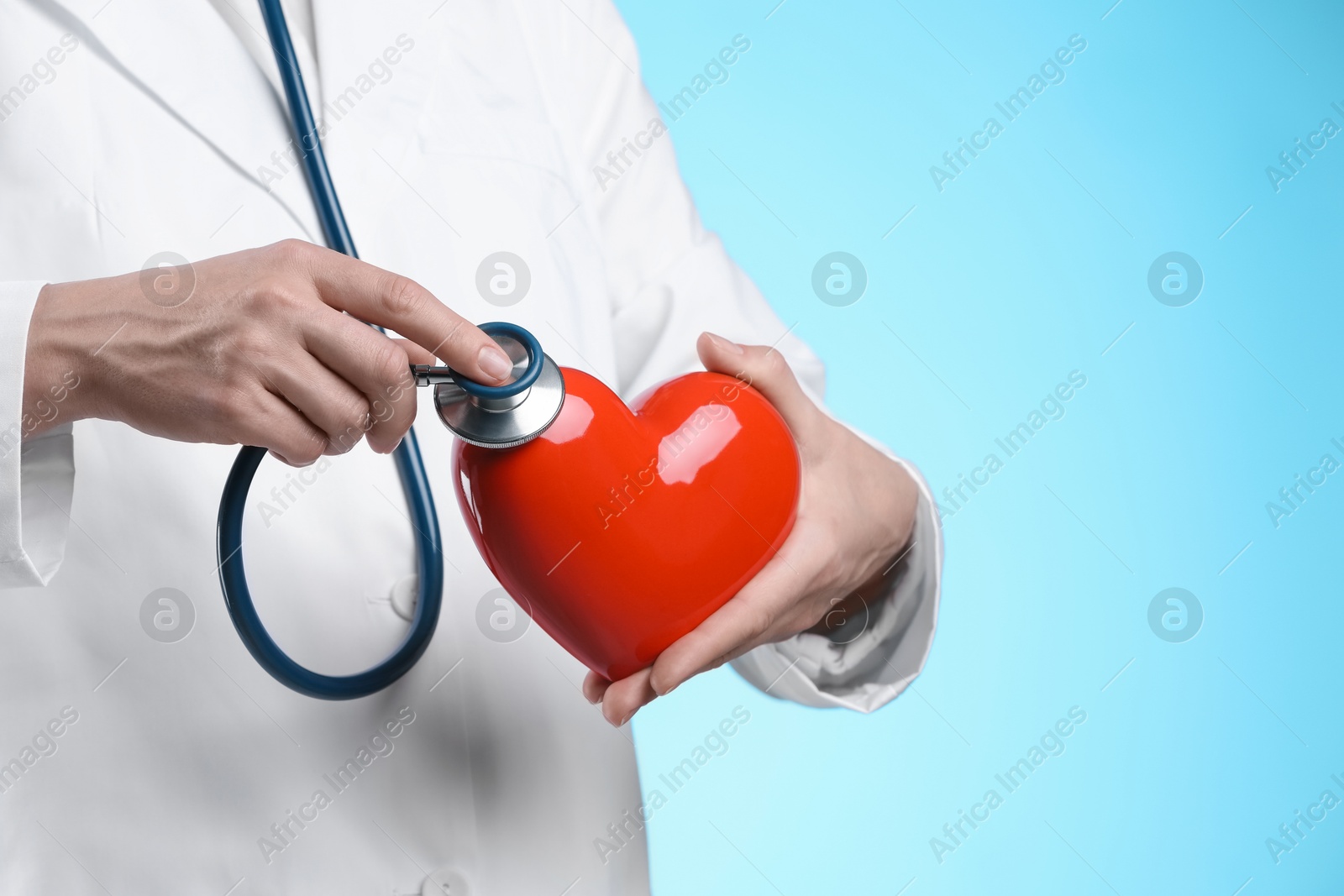 Photo of Doctor with stethoscope and red heart on light blue background, closeup. Space for text