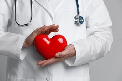 Doctor with red heart on grey background, closeup