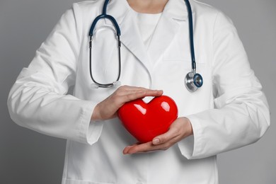 Doctor with red heart on grey background, closeup