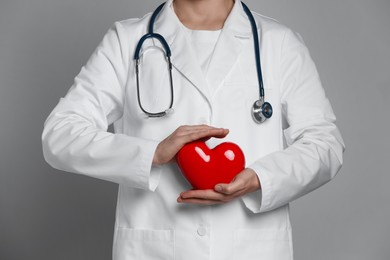 Photo of Doctor with red heart on grey background, closeup