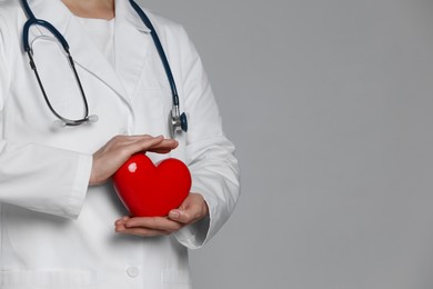 Photo of Doctor with red heart on grey background, closeup. Space for text