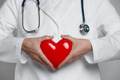 Doctor with red heart on grey background, closeup