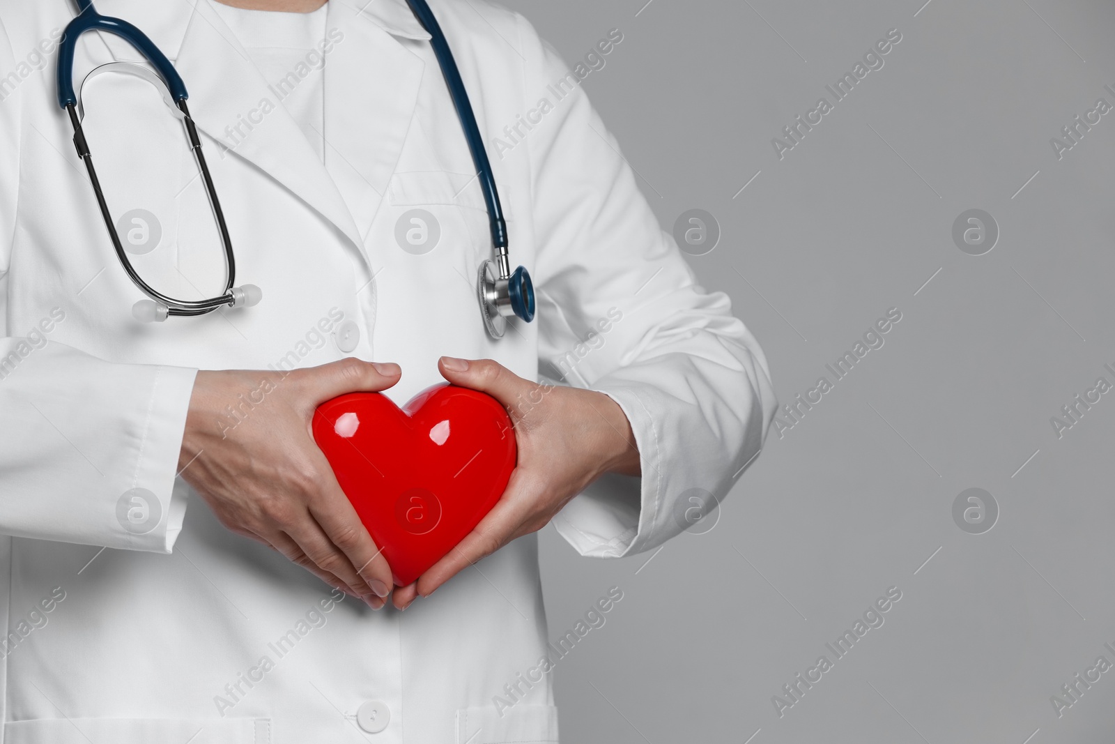 Photo of Doctor with red heart on grey background, closeup. Space for text