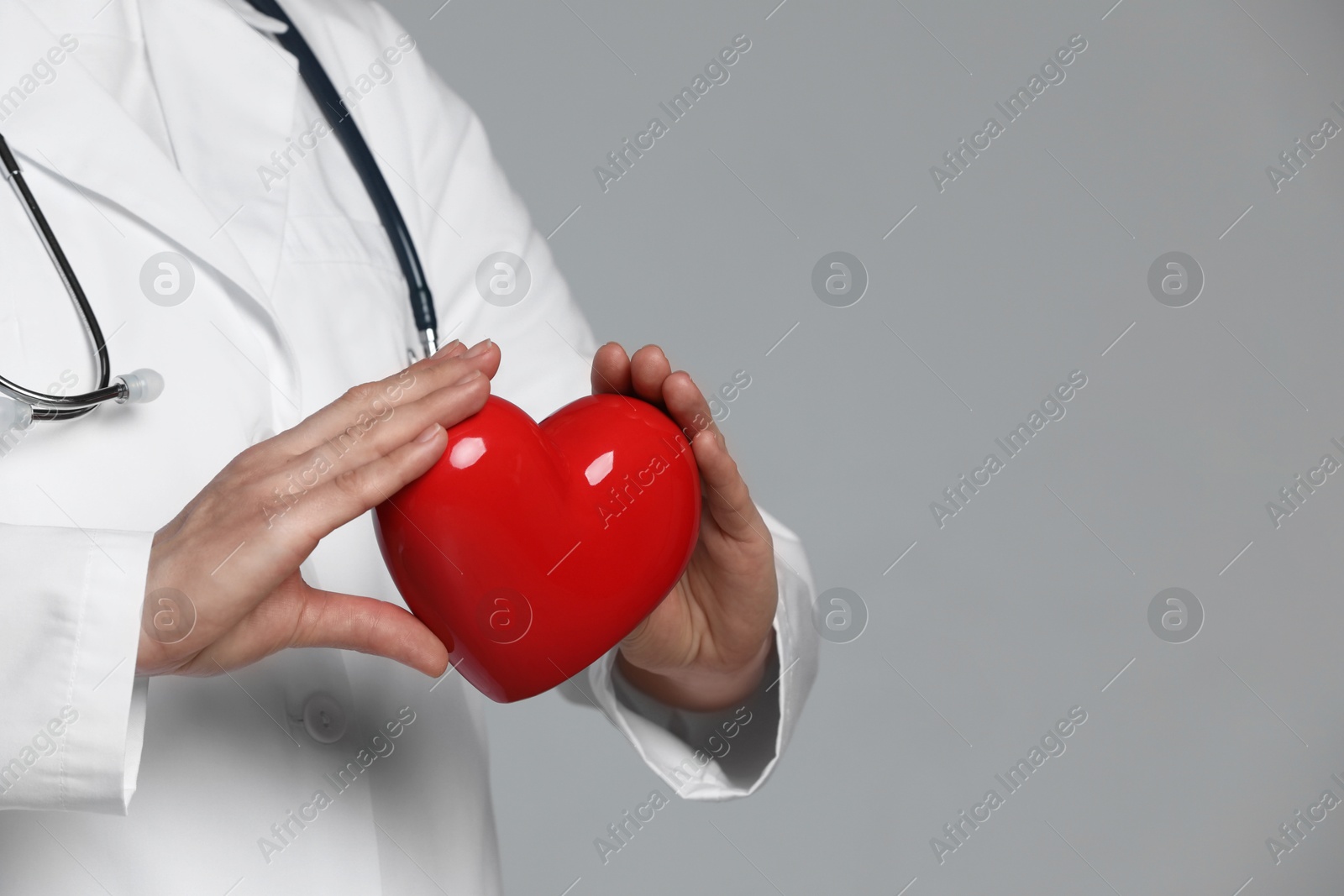 Photo of Doctor with red heart on grey background, closeup. Space for text