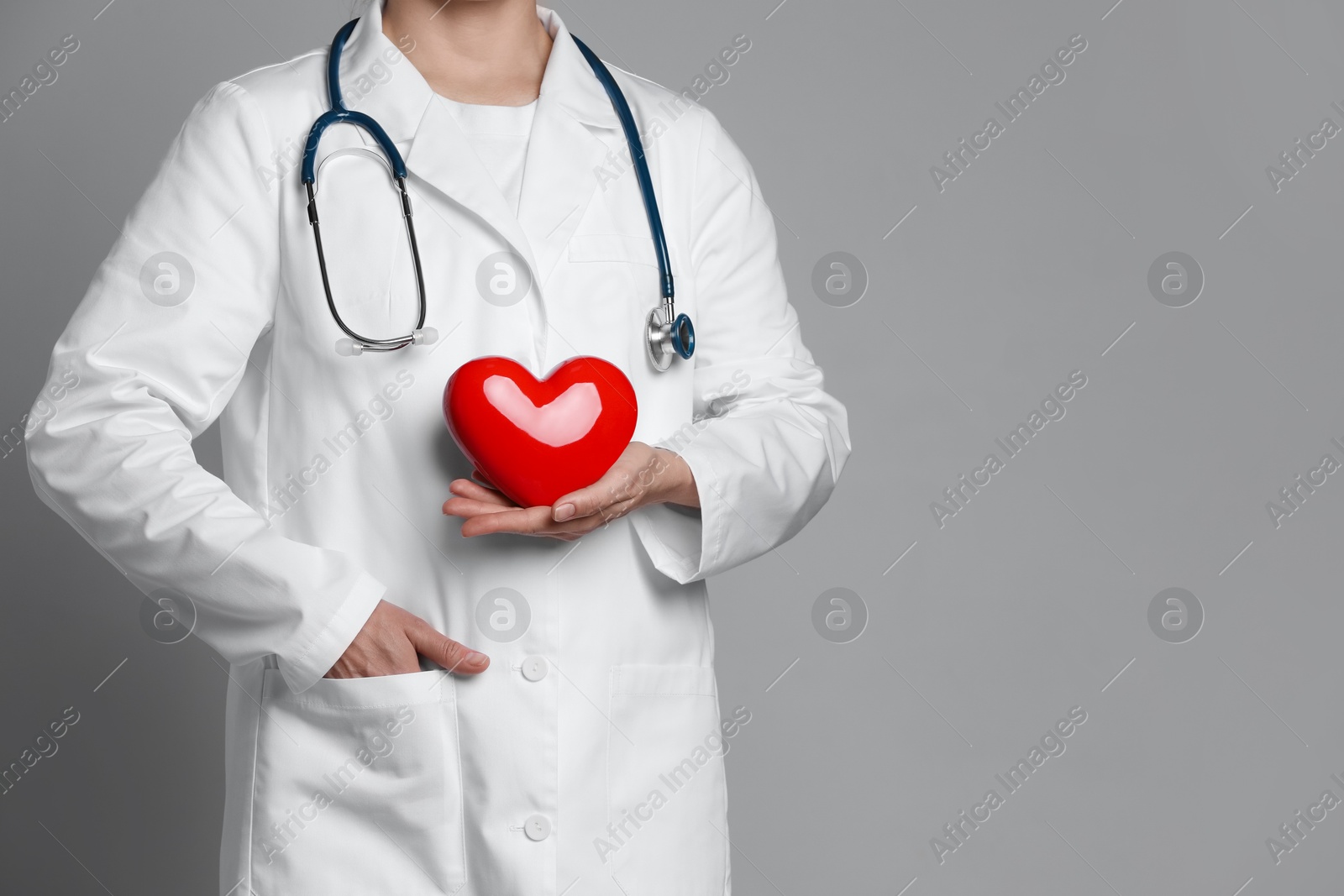 Photo of Doctor with red heart on grey background, closeup. Space for text