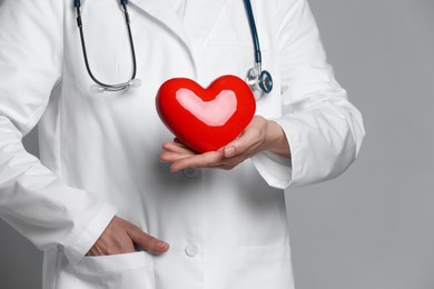 Photo of Doctor with red heart on grey background, closeup