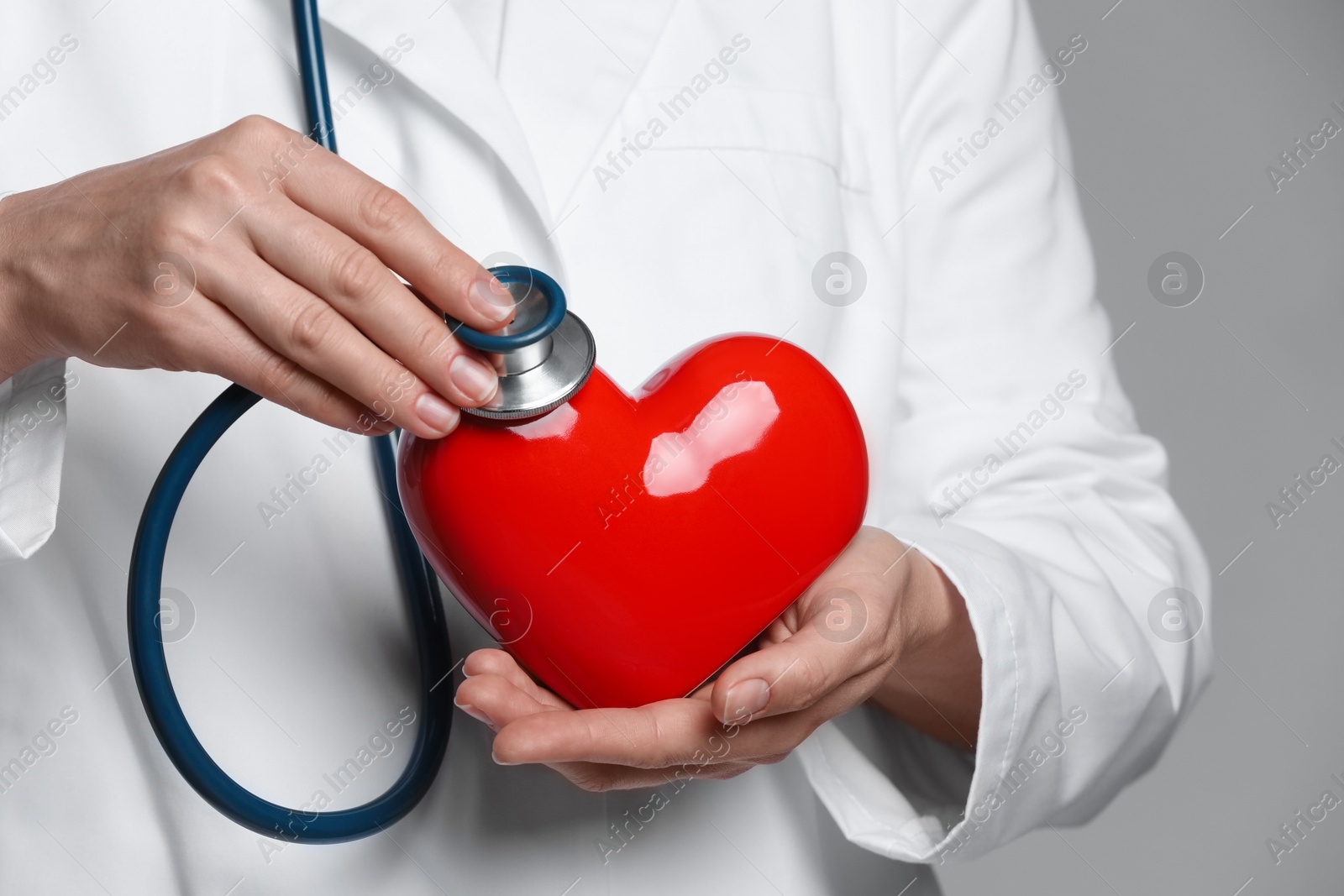 Photo of Doctor with stethoscope and red heart on grey background, closeup