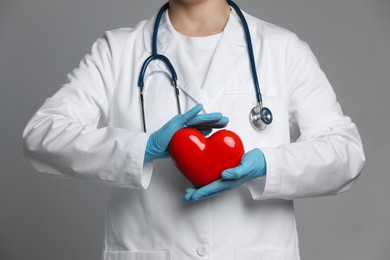 Doctor with red heart on grey background, closeup