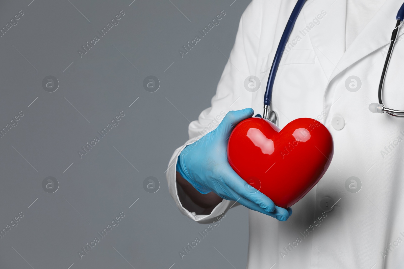 Photo of Doctor with red heart on grey background, closeup. Space for text