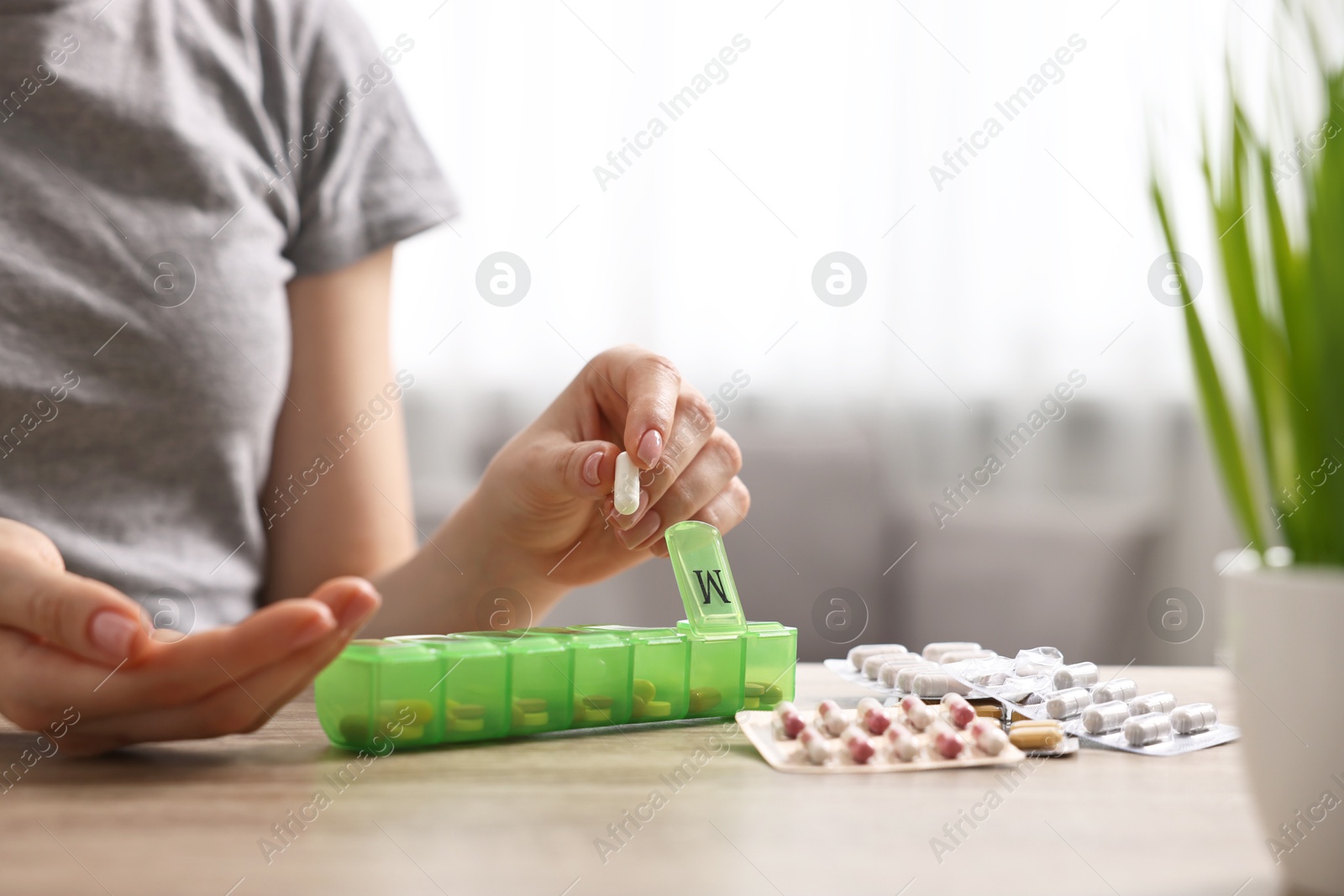 Photo of Woman with pills and organizer at wooden table, closeup