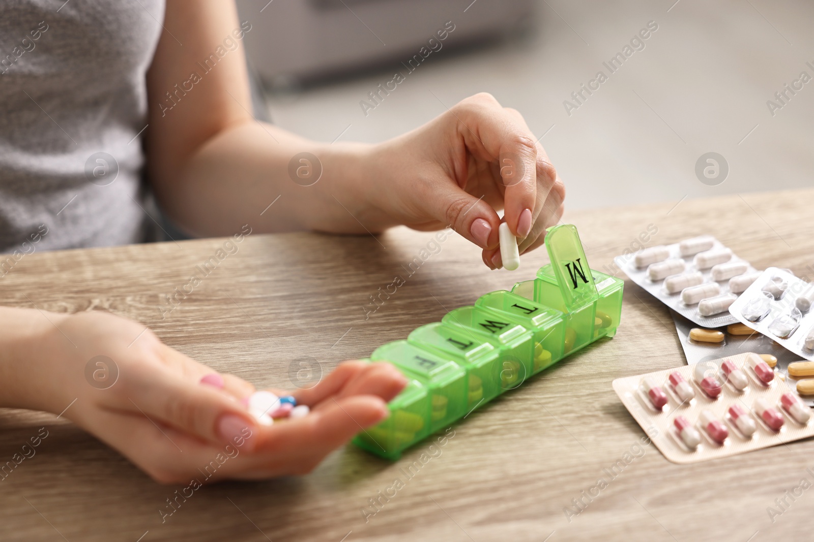 Photo of Woman with pills and organizer at wooden table, closeup