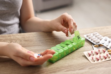 Photo of Woman with pills and organizer at wooden table, closeup