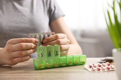 Photo of Woman with pills and organizer at wooden table, closeup