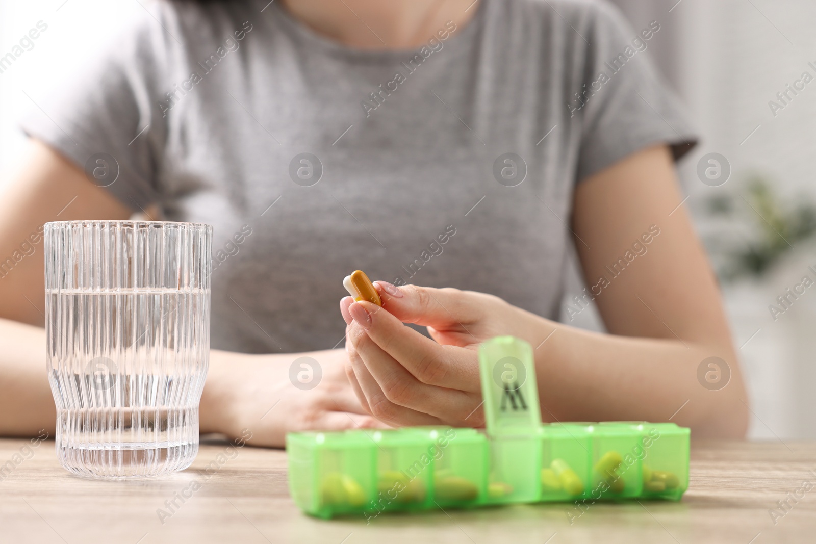 Photo of Woman with pills, organizer and glass of water at wooden table, closeup