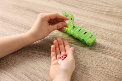 Photo of Woman with pills and organizer at wooden table, closeup