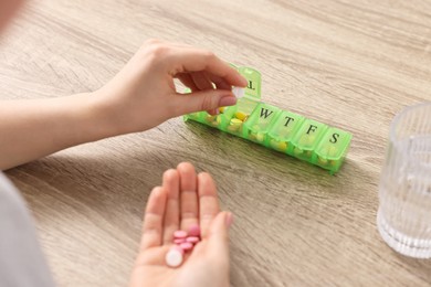 Photo of Woman with pills, organizer and glass of water at wooden table, closeup