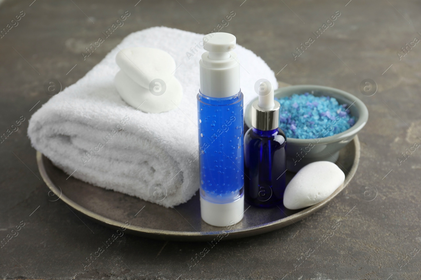 Photo of Spa composition. Cosmetic products, terry towel and sea salt on gray table