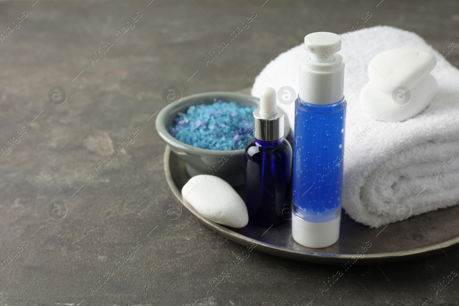 Photo of Spa composition. Cosmetic products, terry towel and sea salt on gray table