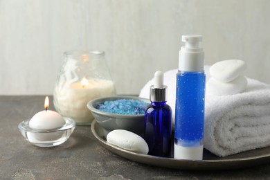 Photo of Spa composition. Cosmetic products, terry towel, burning candles and sea salt on gray table against light background