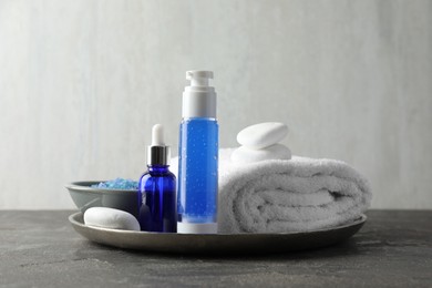 Photo of Spa composition. Cosmetic products, terry towel and sea salt on gray table against light background