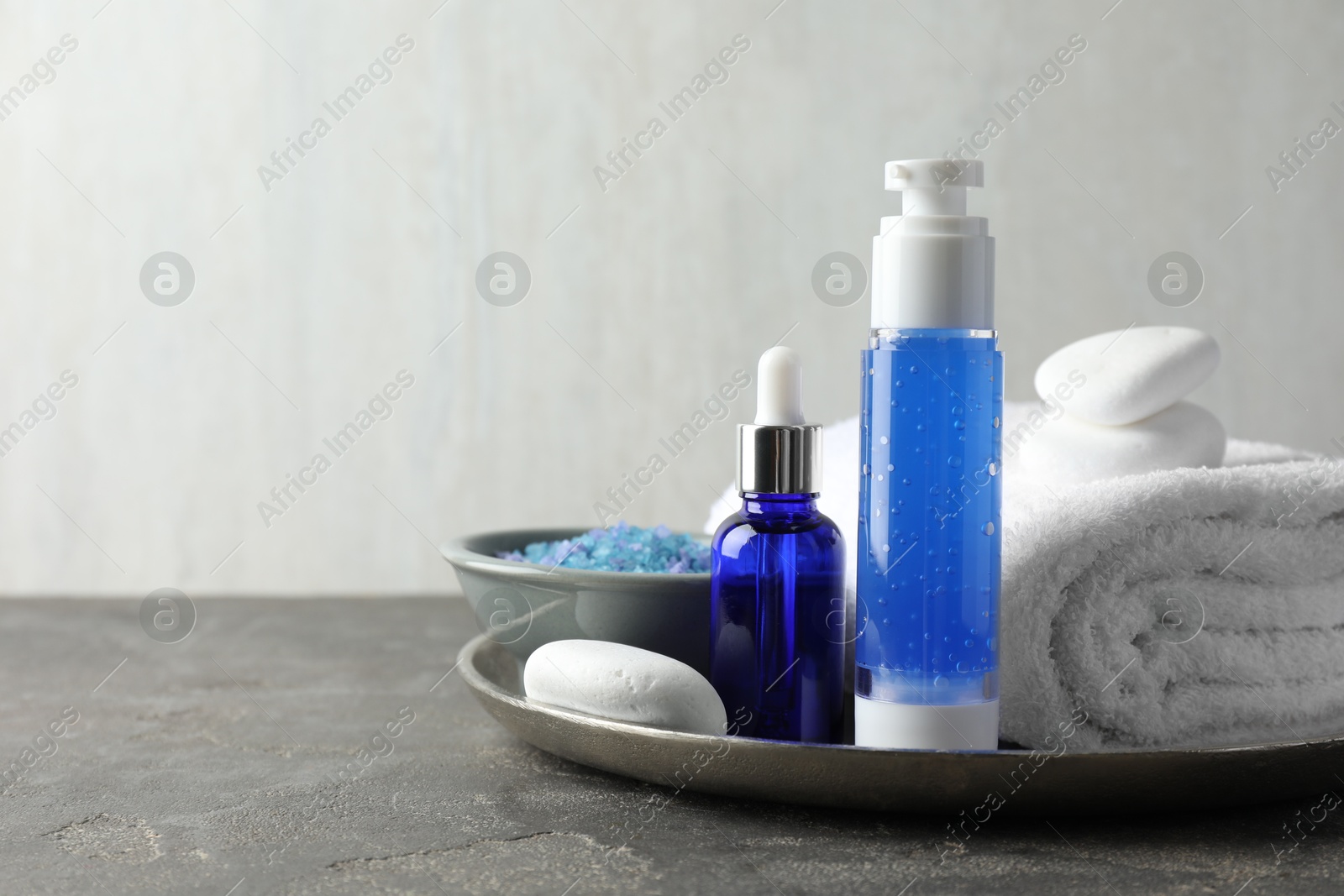 Photo of Spa composition. Cosmetic products, terry towel and sea salt on gray table against light background, space for text