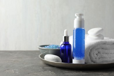 Photo of Spa composition. Cosmetic products, terry towel and sea salt on gray table against light background, space for text