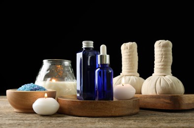 Photo of Spa composition. Cosmetic products, herbal bags, burning candles and sea salt on wooden table against black background