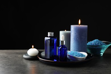 Photo of Spa composition. Cosmetic products, burning candles and sea salt on gray table against black background, space for text