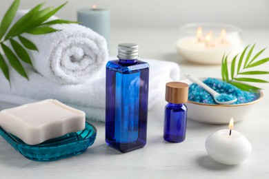 Photo of Spa composition. Cosmetic products, soap, towels, sea salt and burning candles on light table