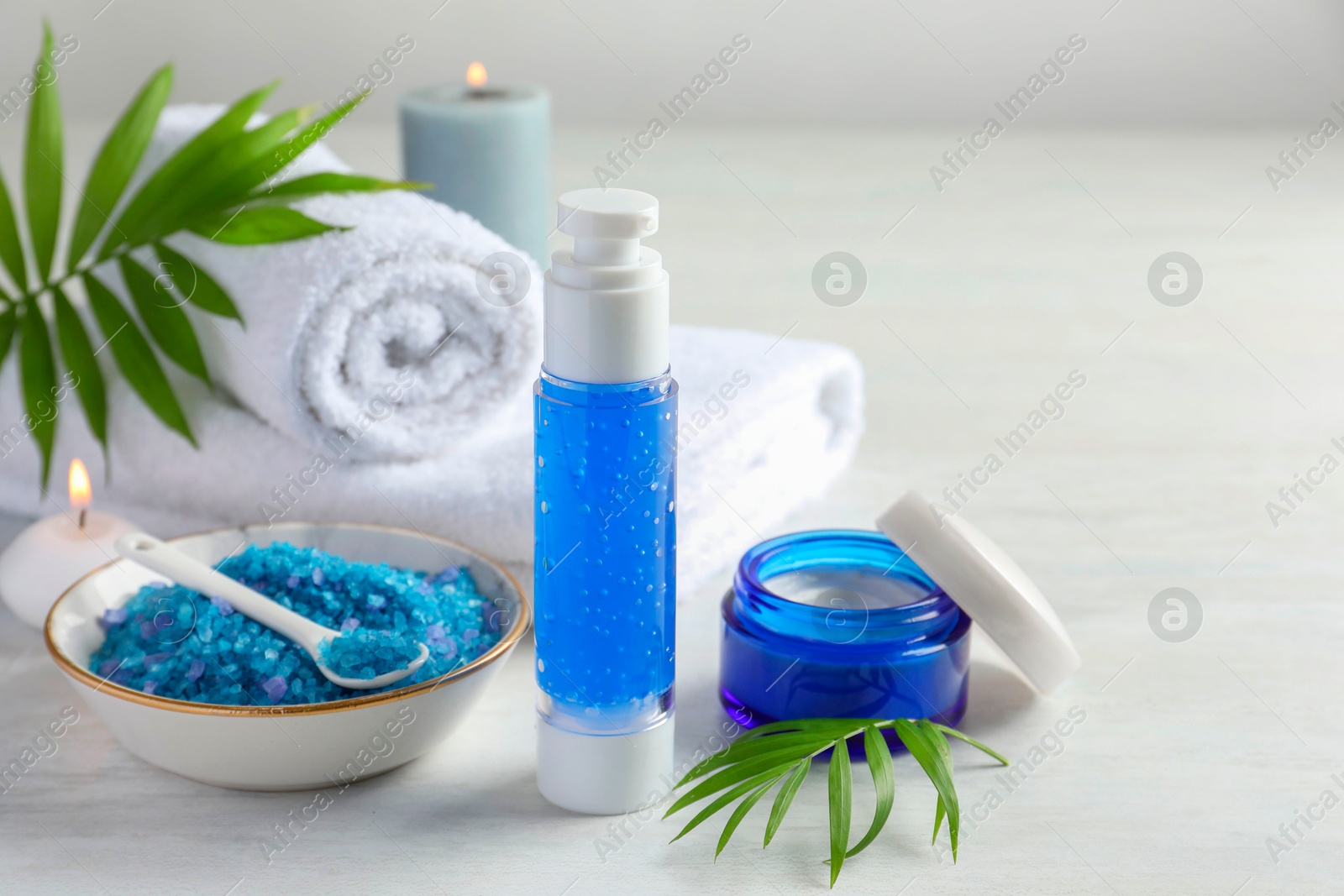 Photo of Spa composition. Cosmetic products, towels, sea salt and burning candles on light table