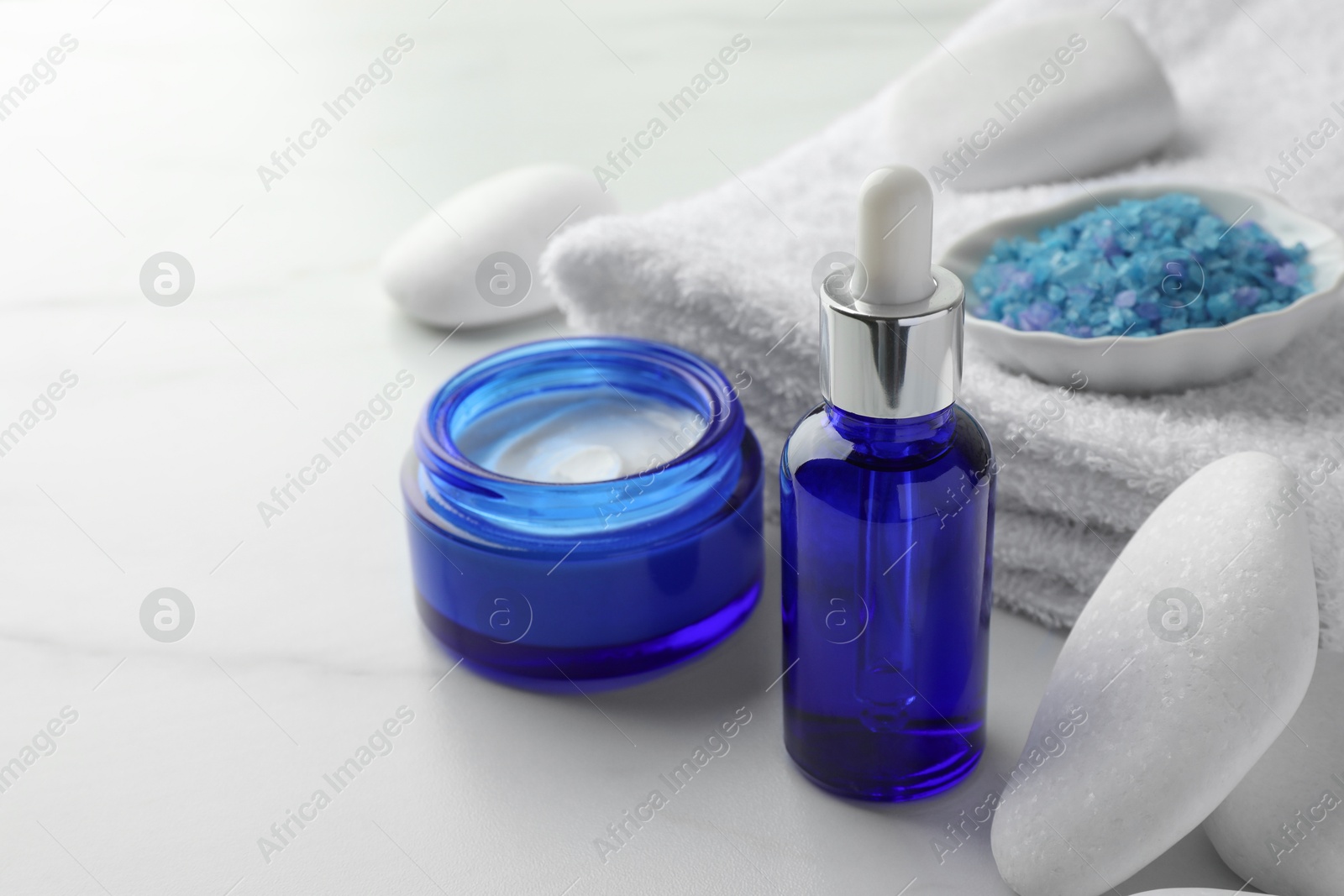 Photo of Spa composition. Cosmetic products, sea salt, towel and stones on white marble table, closeup. Space for text