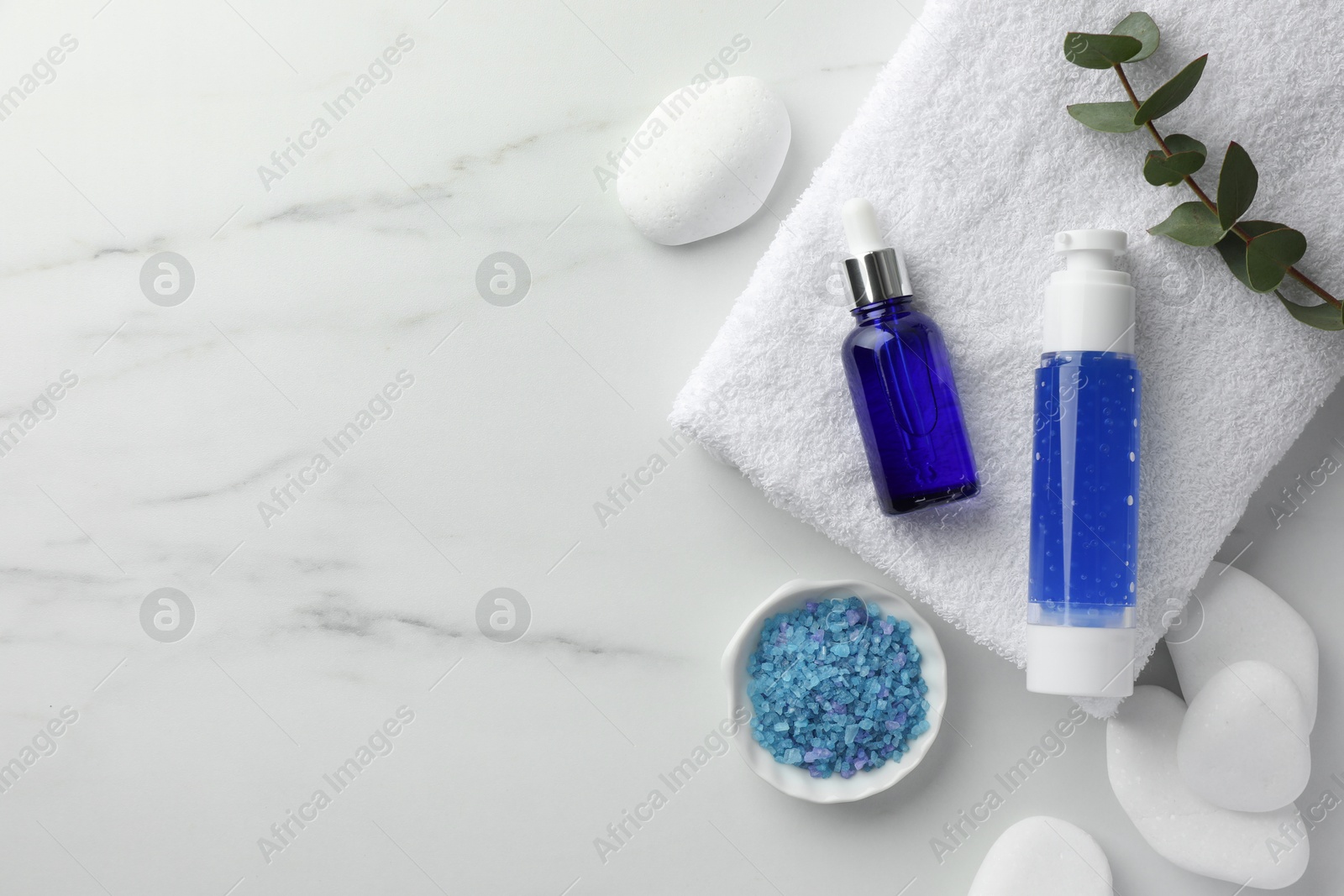 Photo of Spa composition. Bottles of cosmetic products, sea salt, eucalyptus, towel and stones on white marble table, top view. Space for text