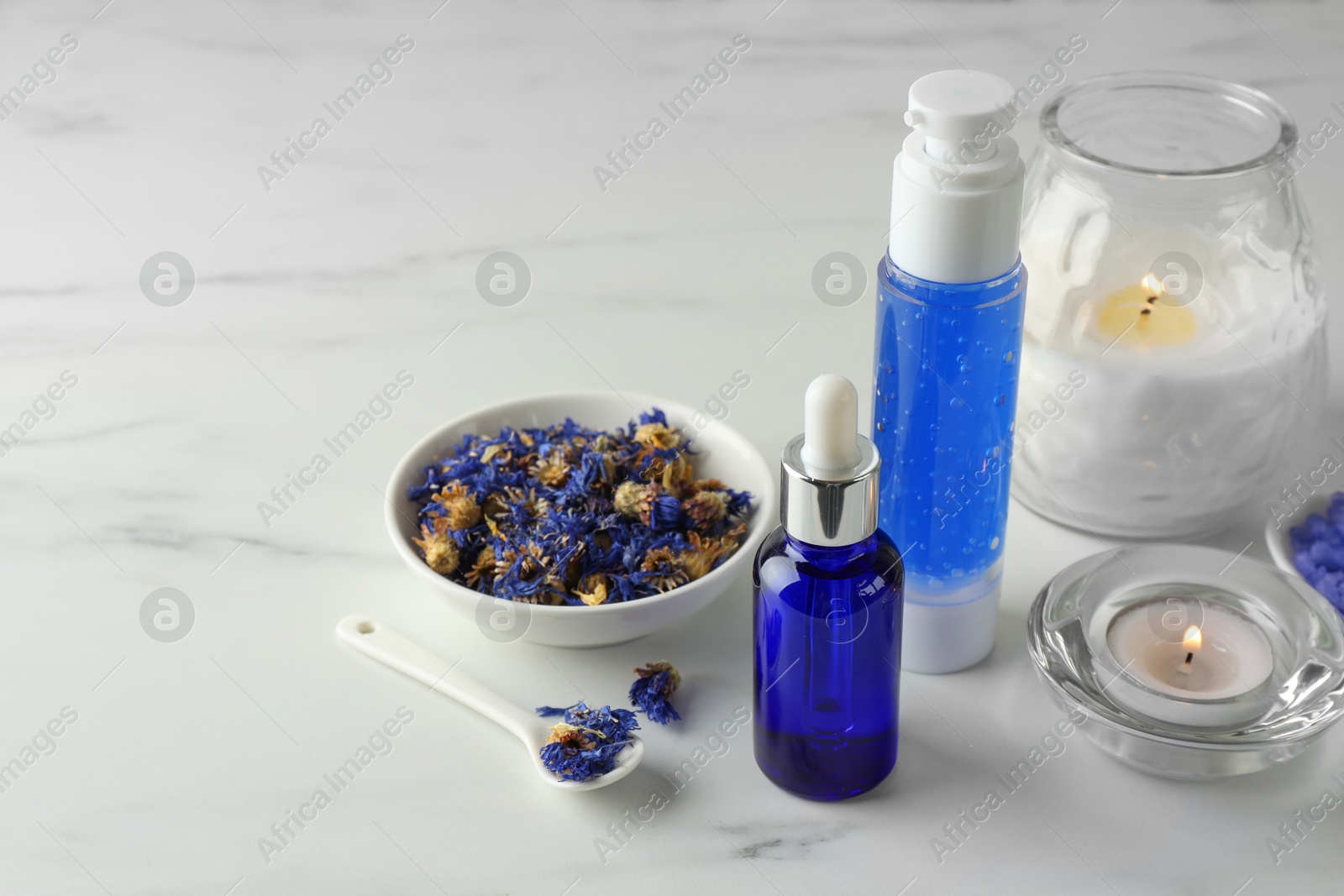 Photo of Spa composition. Bottles of cosmetic products, dry flowers and burning candles on white marble table, space for text