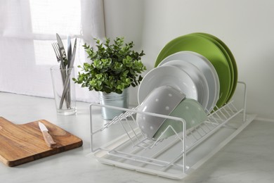 Photo of Drainer with different clean dishware and houseplant on light table in kitchen