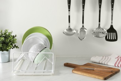 Photo of Drainer with different clean dishware and houseplant on light table in kitchen