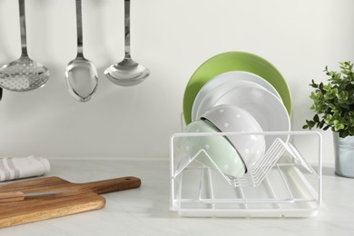 Photo of Drainer with different clean dishware and houseplant on light table in kitchen