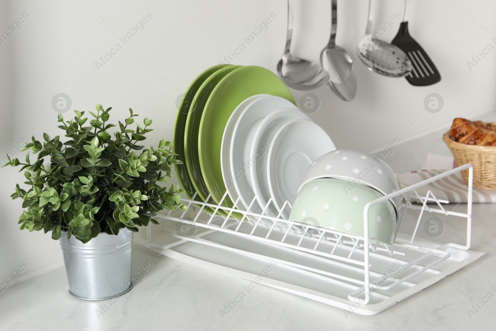 Photo of Drainer with different clean dishware and houseplant on light table in kitchen
