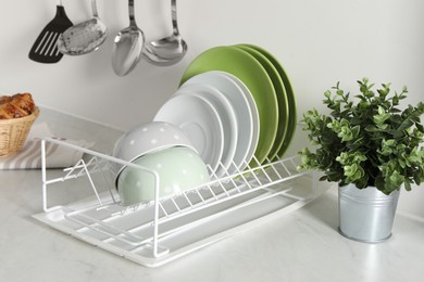 Photo of Drainer with different clean dishware and houseplant on light table in kitchen